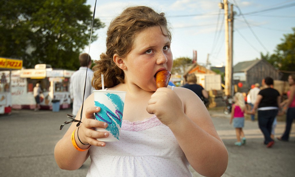 Overweight girl (10-12) holding balloon and eating corndog --- Image by © Richard Schultz/Corbis